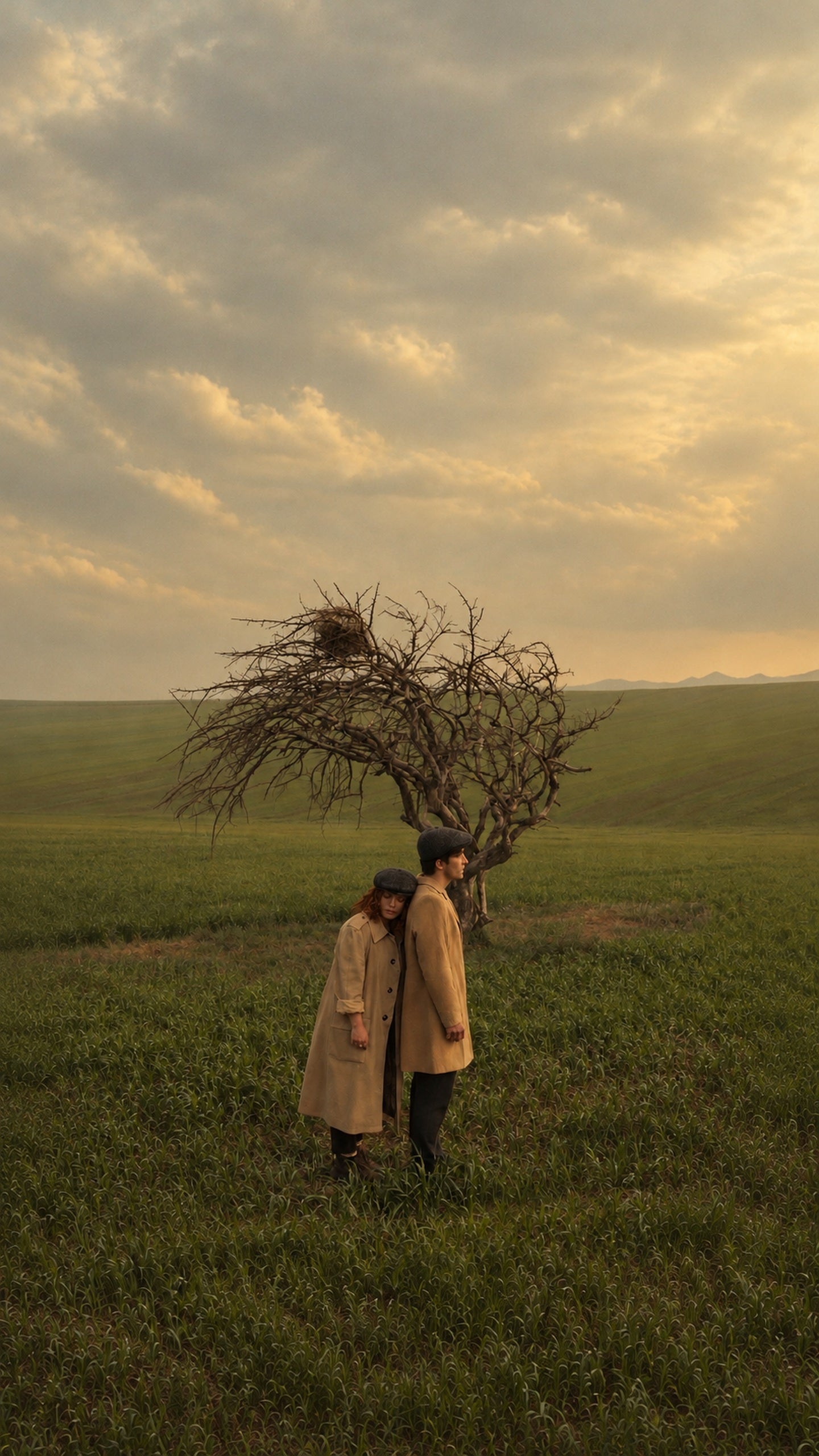 Two people in trench coats in a green field